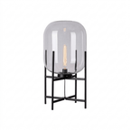 Clear glass shade with a long filament bulb on a black four-leg frame, shown on a plain white background for this Clérachic lamp.