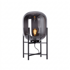 Dark smoked glass shade with a glowing filament bulb on a black four-leg stand, on a plain white background, from Clérachic.