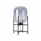 Blue-grey tinted glass shade with a tall filament bulb on a black four-leg frame, this Clérachic lamp on a plain white backdrop.