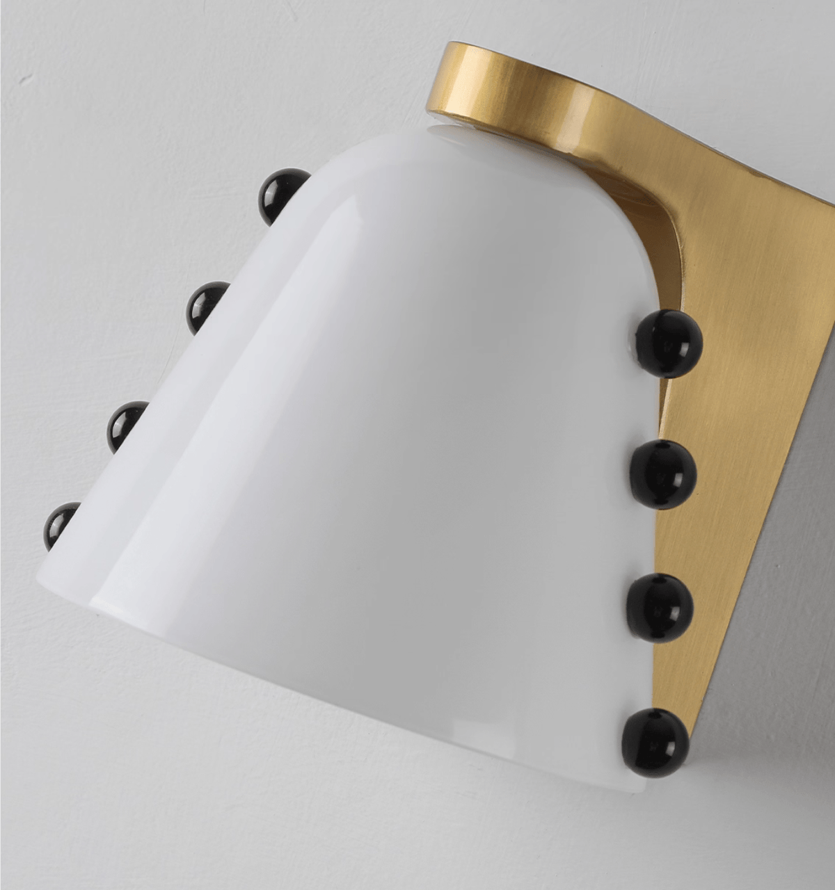 Close view of the white glass shade, its gold bracket and the row of black glass studs on both sides; a Clérachic wall sconce.
