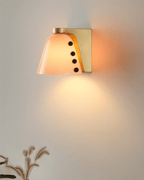 Peach-orange glass shade glowing against a warm wall, with a few dried stems below it; a Clérachic wall sconce.