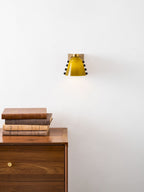 Small green glass sconce high on a white wall above a walnut cabinet and a pile of old books; a Clérachic wall light.