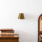 Compact green sconce on a white wall with books on a walnut cabinet and the edge of an arched frame at right; a Clérachic wall light.