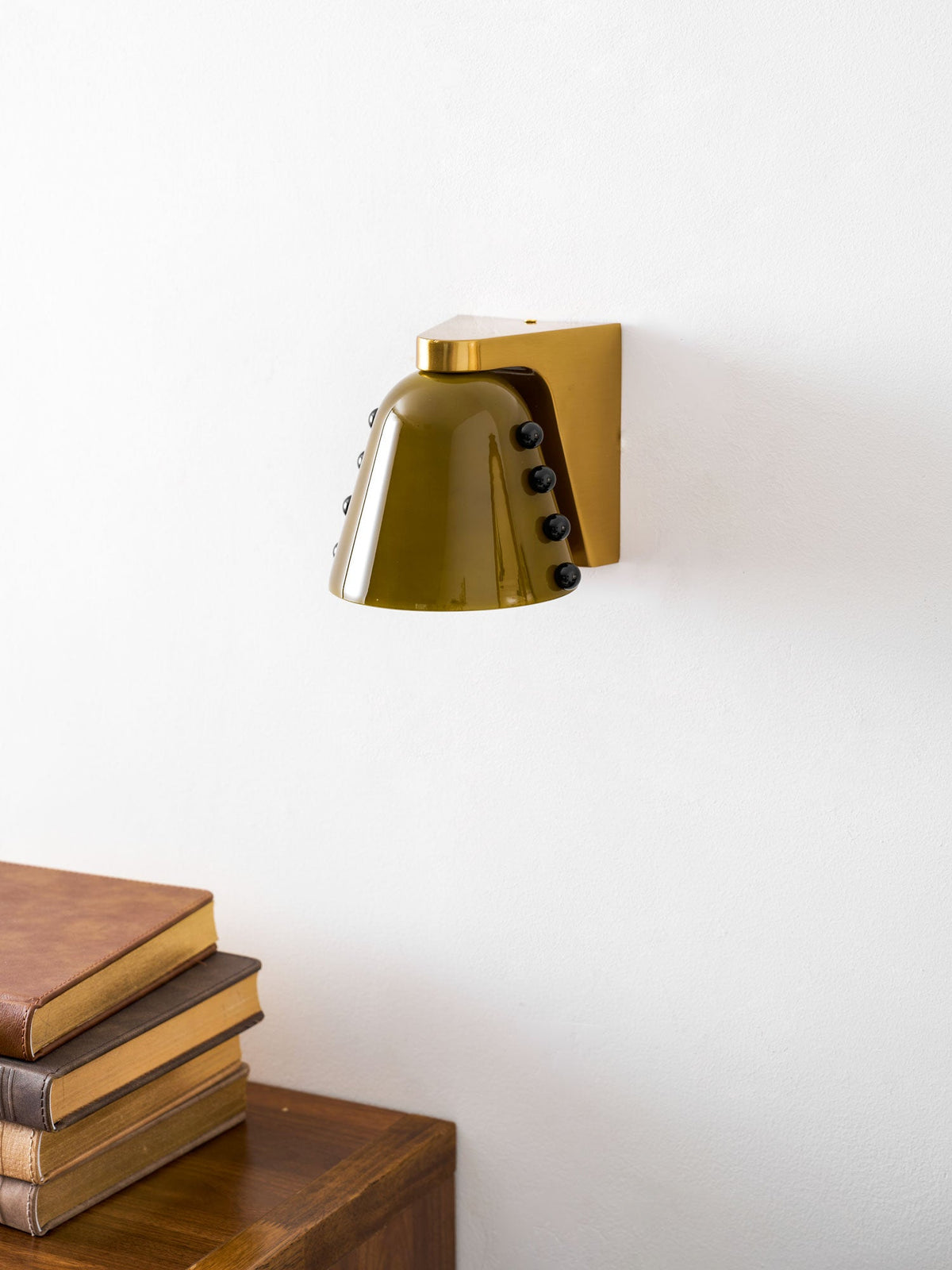 Angled view of the green glass shade and gold bracket, with a book stack at the lower left; a Clérachic wall sconce.