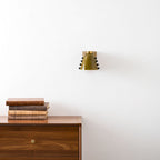 The green wall light centred on a white wall above a walnut drawer unit with a brass knob; a Clérachic design.