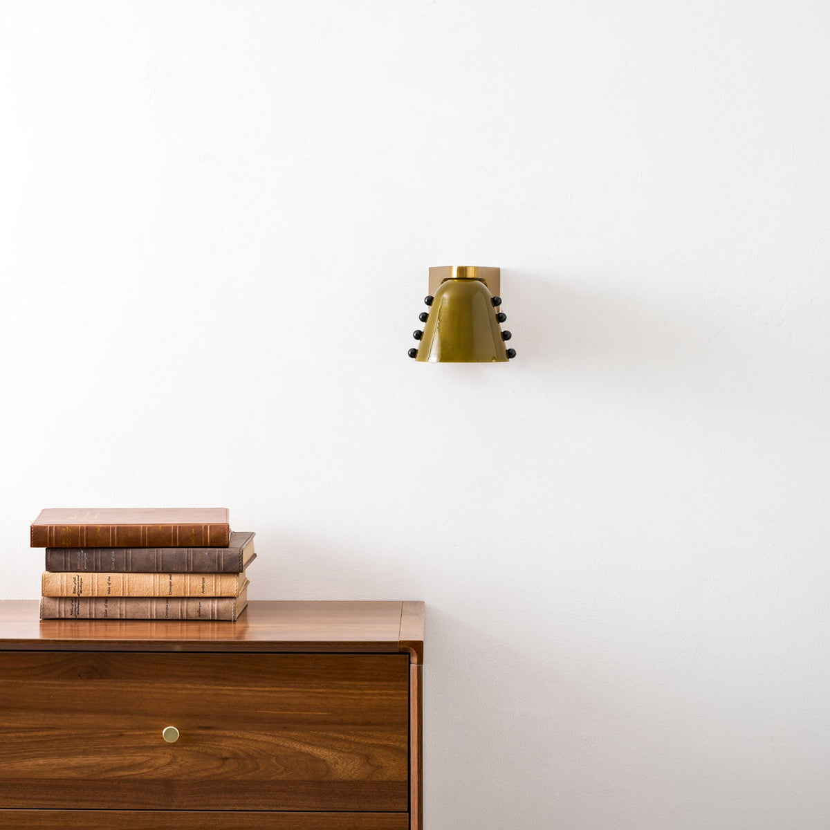 The green wall light centred on a white wall above a walnut drawer unit with a brass knob; a Clérachic design.