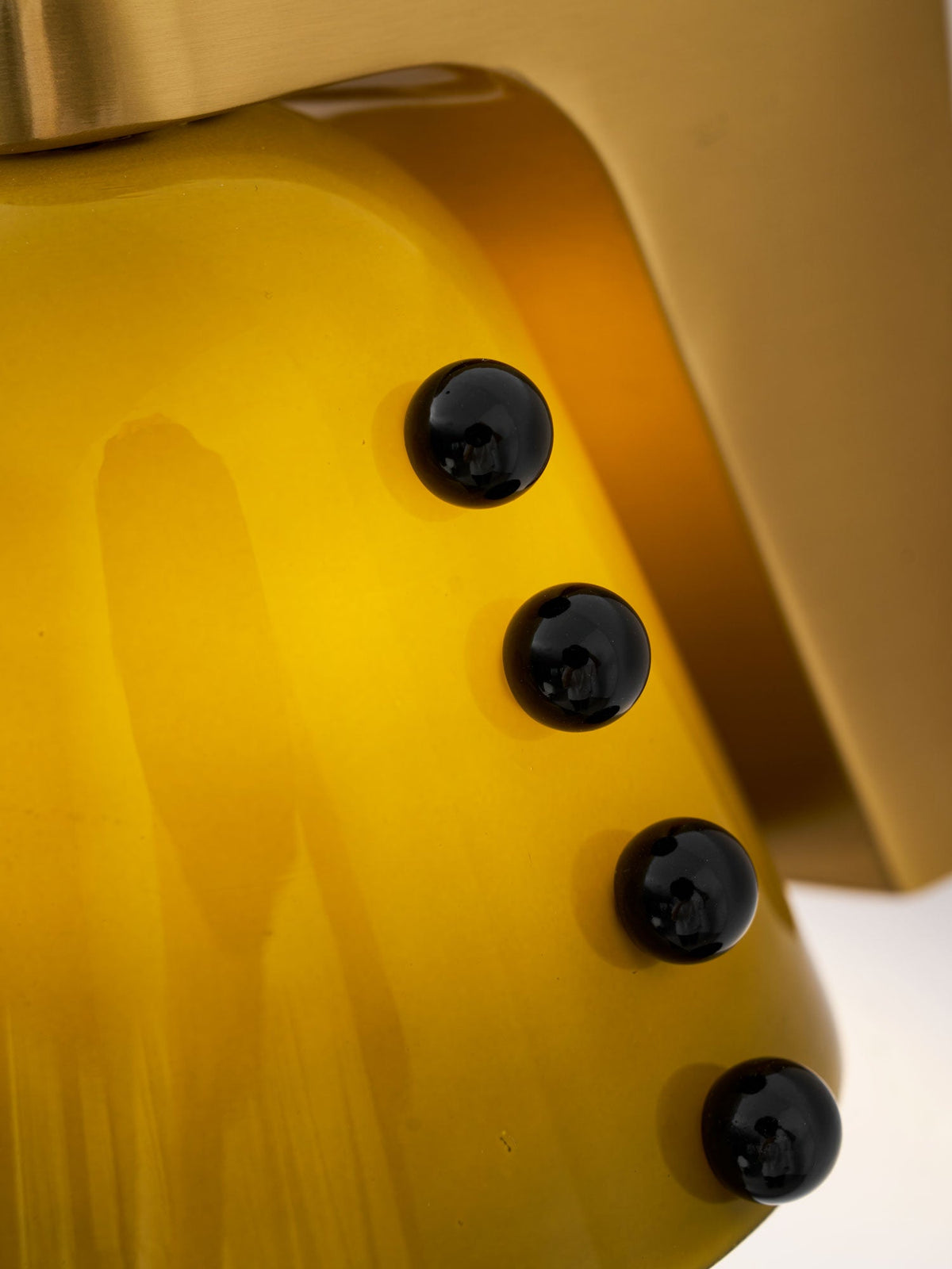 Macro view of green glass with streaks of colour, four black studs and the brushed gold bracket of this Clérachic wall light.