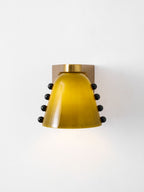 Front view of the lit green glass shade with black studs on each side and a round gold cap; a Clérachic wall sconce.