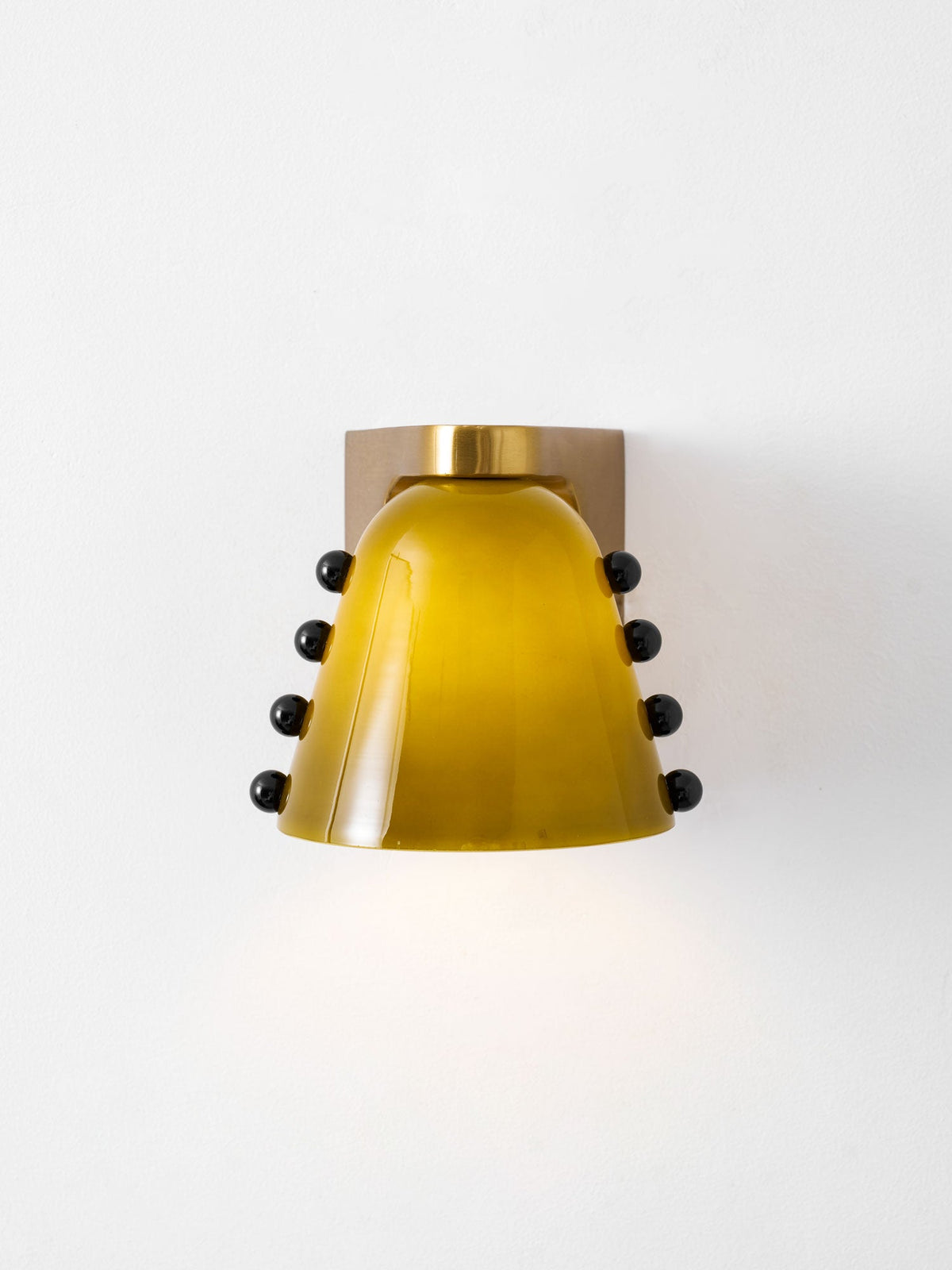 Front view of the lit green glass shade with black studs on each side and a round gold cap; a Clérachic wall sconce.