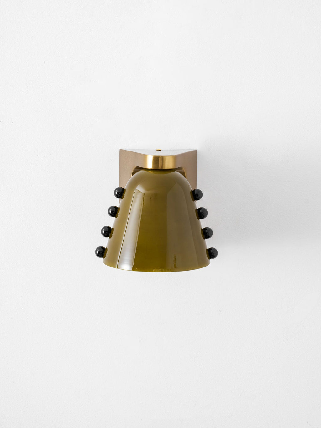 Green glass wall light with studs on both sides, seen straight on, on a white wall; a Clérachic design.