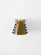 Green glass wall light with studs on both sides, seen straight on, on a white wall; a Clérachic design.