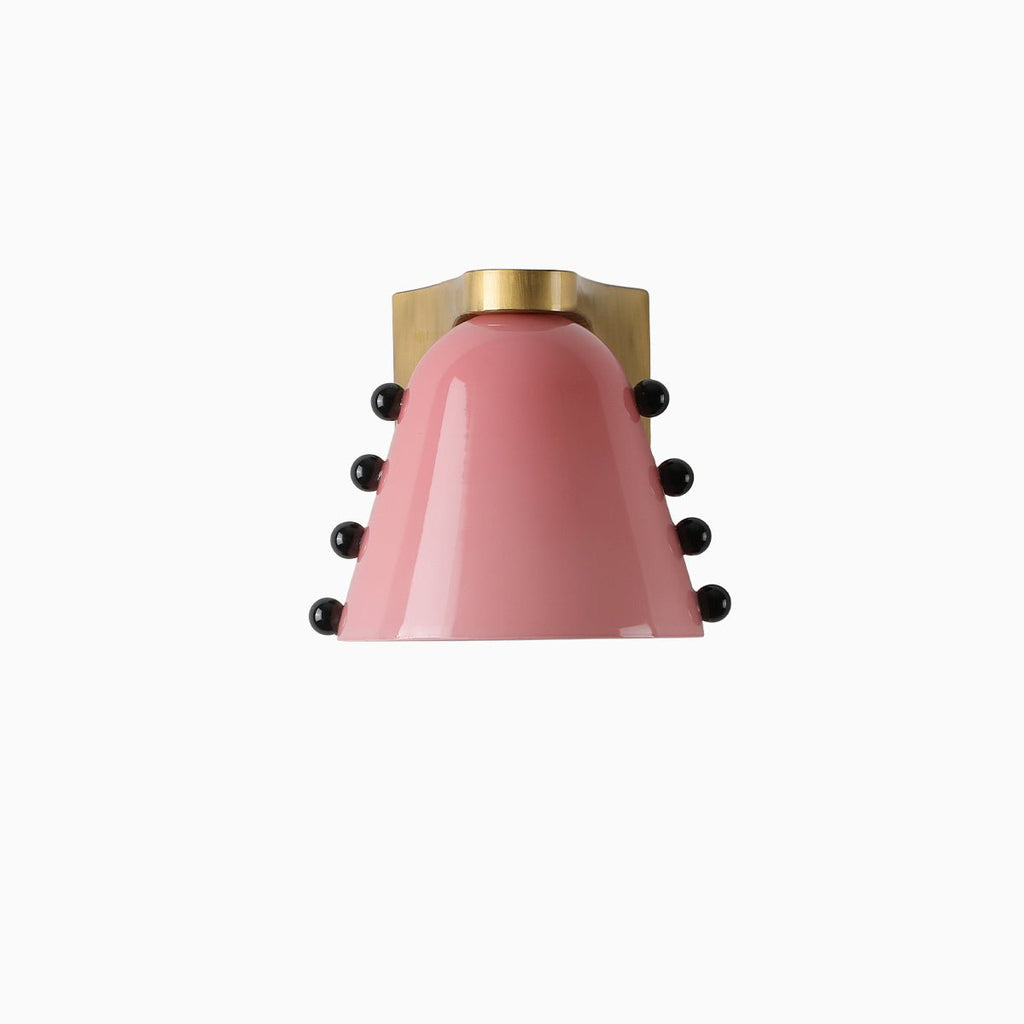 Pink glass version of the wall light with black studs and a gold bracket, on a pale background; from Clérachic.