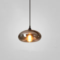 Clérachic hand-blown smoked glass pendant with a wide flattened disc shade, lit and hung on a black cord.