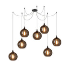 Seven globe Clérachic smoked glass pendants on a seven-cord canopy, clustered at mixed drop heights.