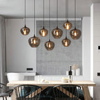 Nine apple-bowl Clérachic smoked glass pendants lighting a wooden dining table against a concrete panel.