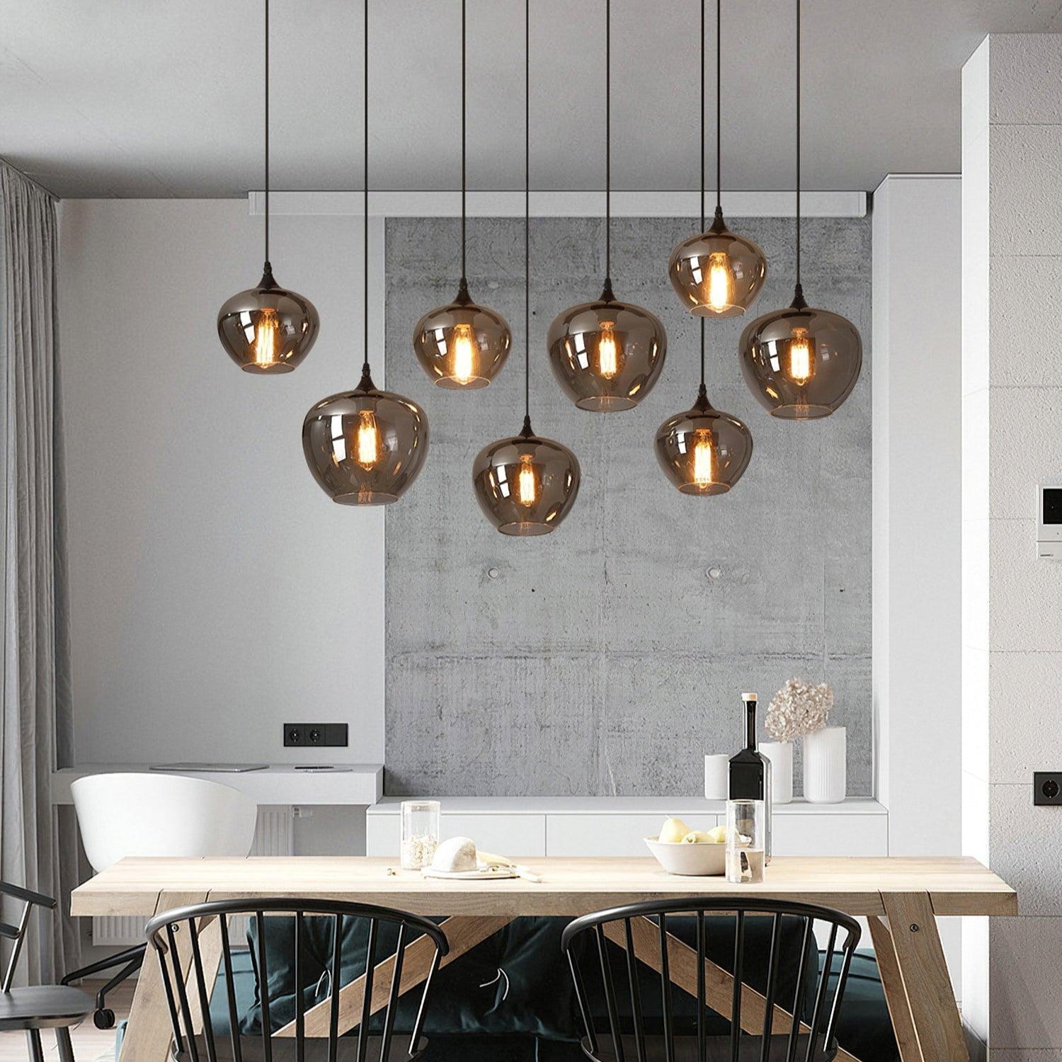 Nine apple-bowl Clérachic smoked glass pendants lighting a wooden dining table against a concrete panel.