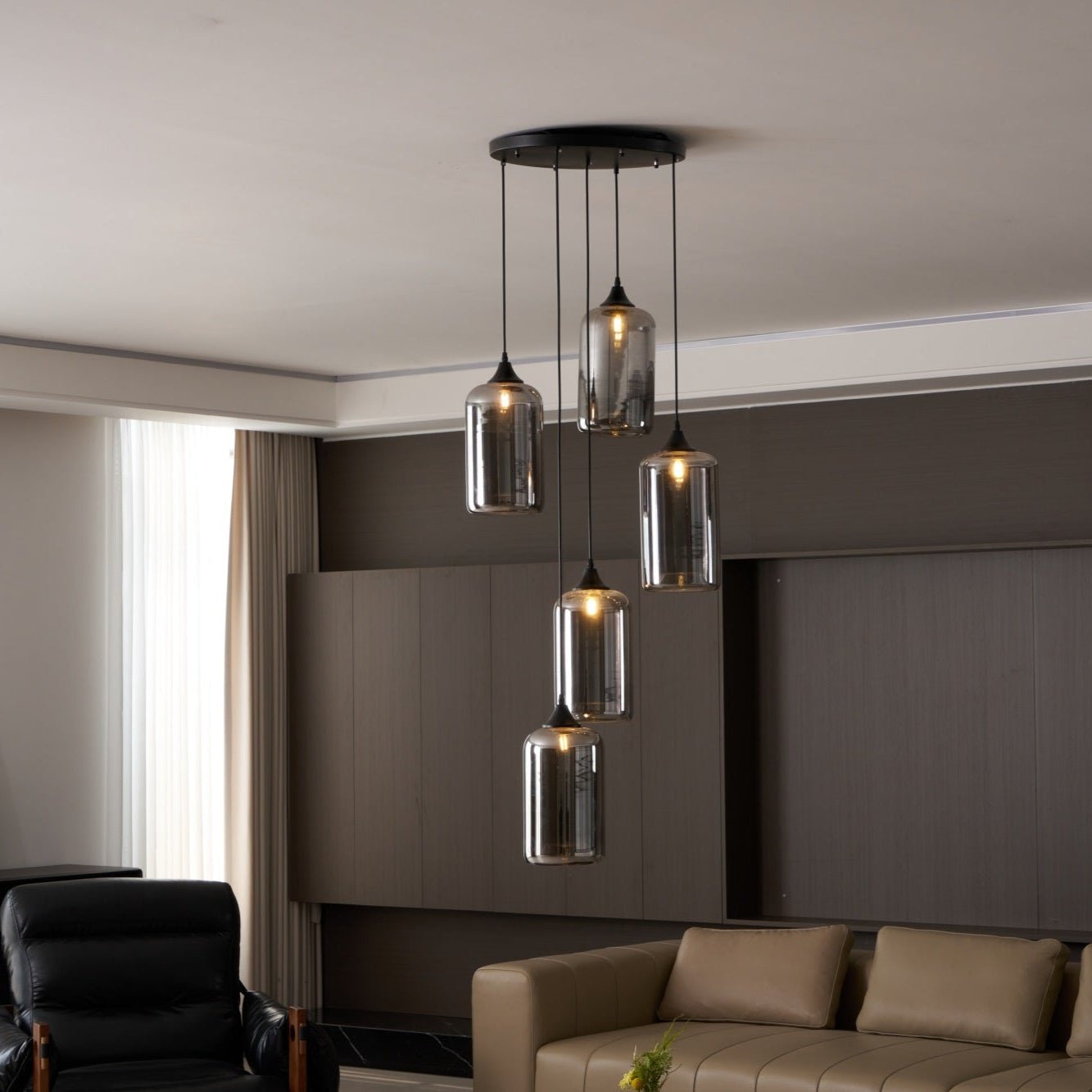 Five cylinder Clérachic smoked glass pendants on a round canopy above a tan sofa in a panelled living room.