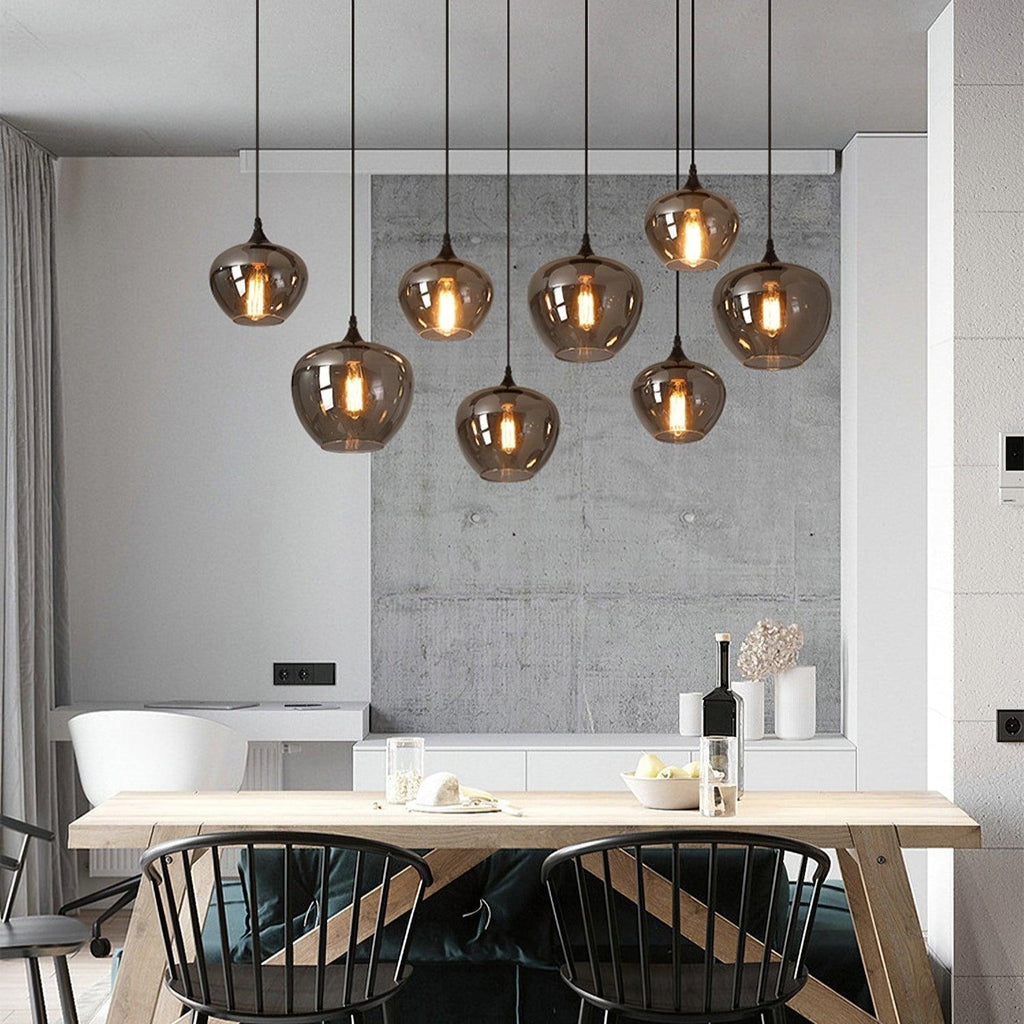 Nine apple-bowl Clérachic smoked glass pendants over a dining table set with wine, fruit and a vase.
