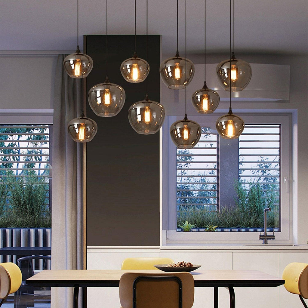 Nine apple-bowl Clérachic smoked glass pendants lighting a dining table beside a garden-facing window.