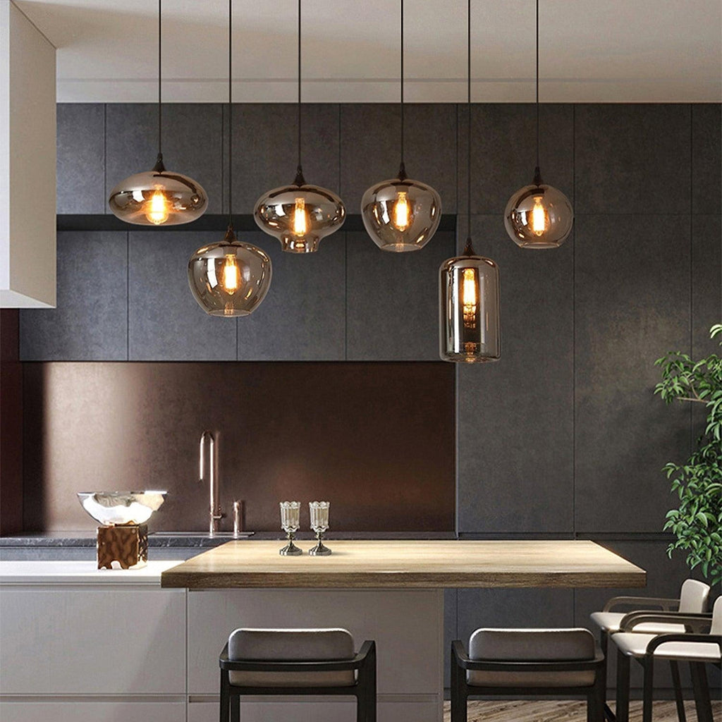 Six mixed-shape Clérachic smoked glass pendants strung above a kitchen island against dark tile.