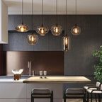 Six mixed-shape Clérachic smoked glass pendants strung above a kitchen island against dark tile.