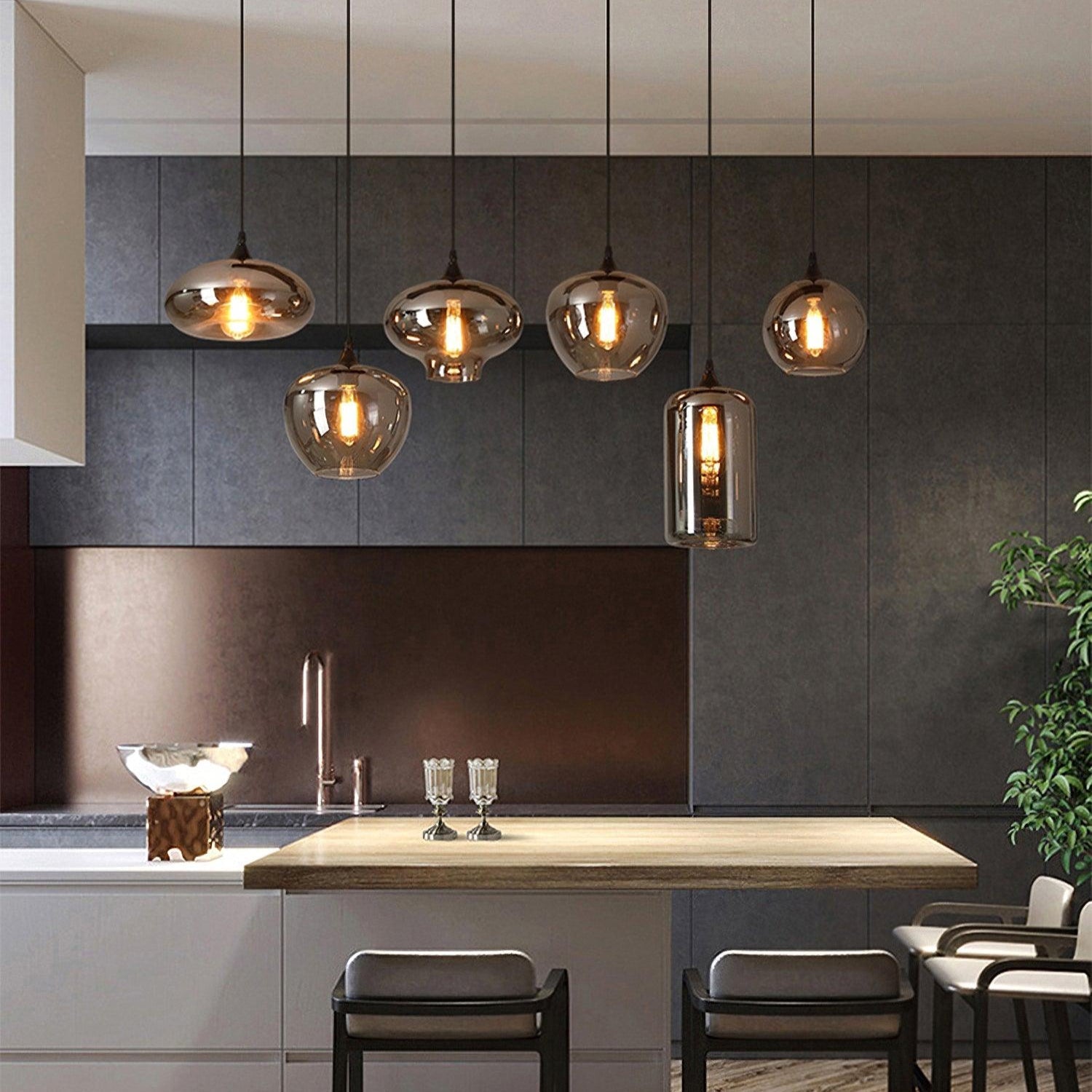 Six mixed-shape Clérachic smoked glass pendants strung above a kitchen island against dark tile.