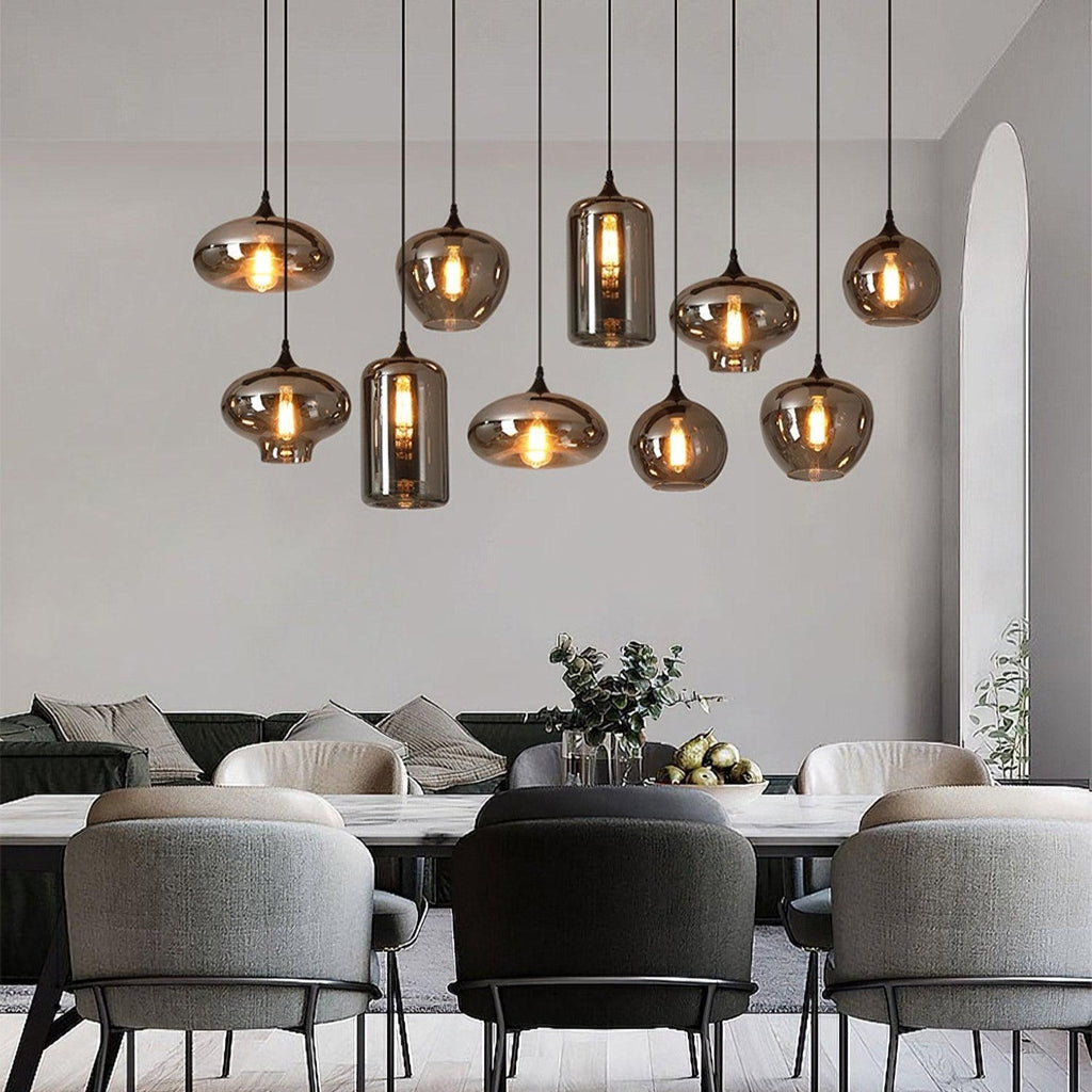 Ten Clérachic smoked glass pendants in mixed shapes over a marble dining table in a pale open-plan room.
