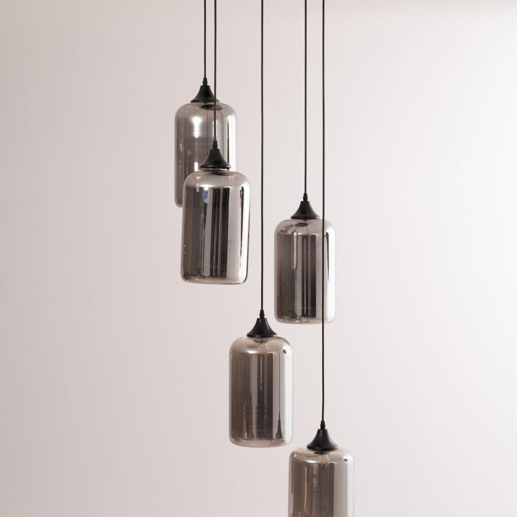 Five Clérachic smoked glass cylinder shades photographed close against a pale wall, cords at mixed drops.