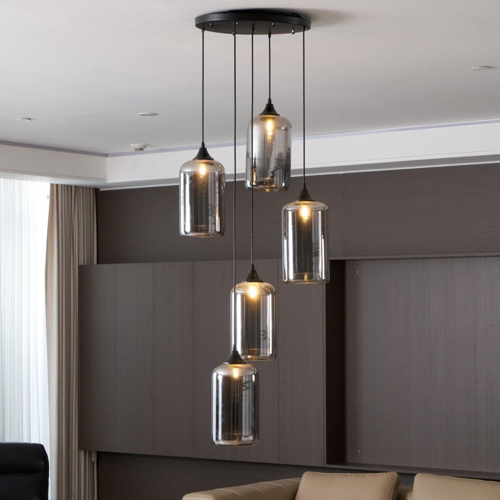 Five cylinder Clérachic smoked glass pendants from a round canopy, lit above a panelled wall and sofa.