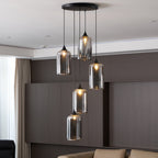 Five cylinder Clérachic smoked glass pendants from a round canopy, lit above a panelled wall and sofa.