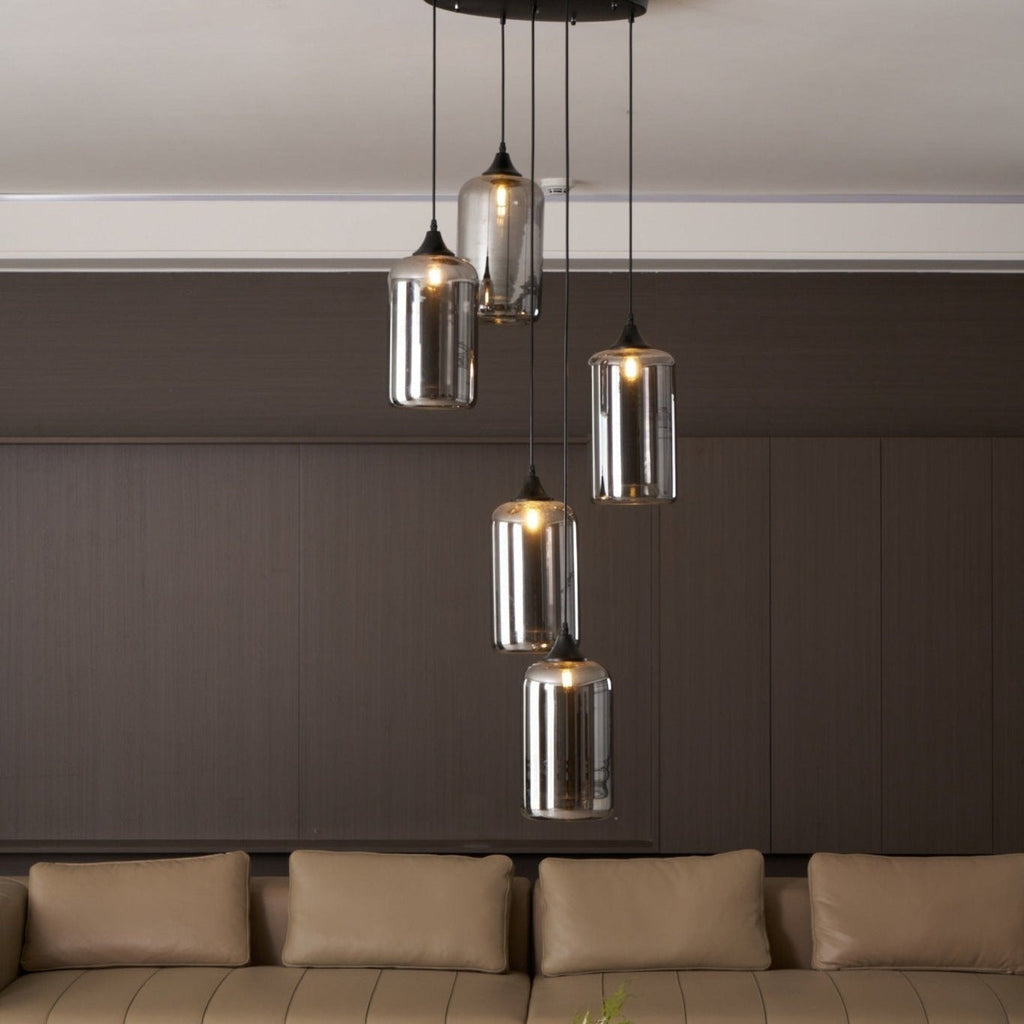Clérachic smoked glass cylinder cluster hung low over a tan leather sofa under a white cornice.
