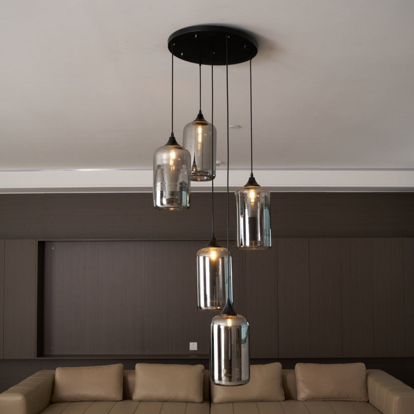 Five Clérachic smoked glass cylinders on a round canopy, hung above a long leather sofa.