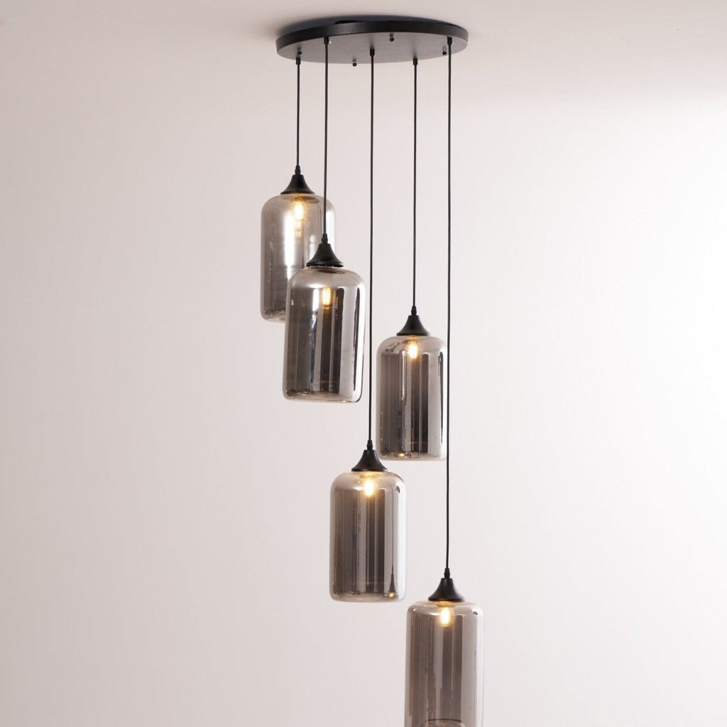 Five Clérachic smoked glass cylinder pendants on a round canopy against a plain painted wall.