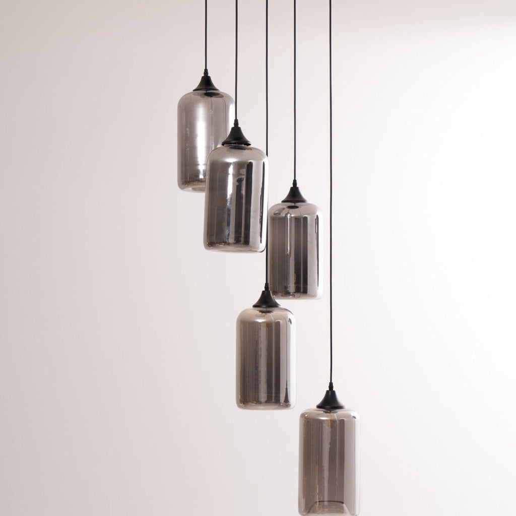Five Clérachic smoked glass cylinders on staggered cords, shades mirrored against a soft grey wall.
