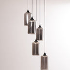 Five Clérachic smoked glass cylinders on staggered cords, shades mirrored against a soft grey wall.