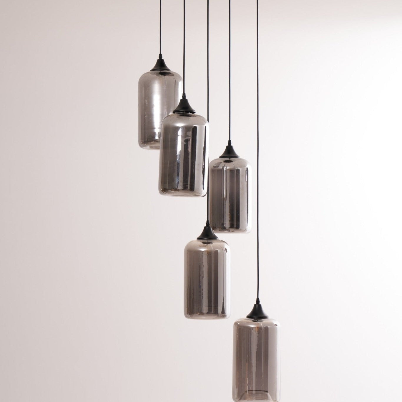 Five Clérachic smoked glass cylinders on staggered cords, shades mirrored against a soft grey wall.