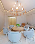 Hung in a pale lounge with round blue-grey armchairs and a wooden table, this copper Clérachic chandelier has many arms tipped with lit leaf shades.