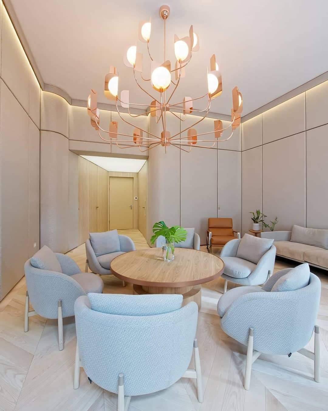 Hung in a pale lounge with round blue-grey armchairs and a wooden table, this copper Clérachic chandelier has many arms tipped with lit leaf shades.