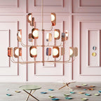 In a pink panelled room, a Clérachic chandelier in a copper finish carries lit globes behind leaf shades above two small side tables.