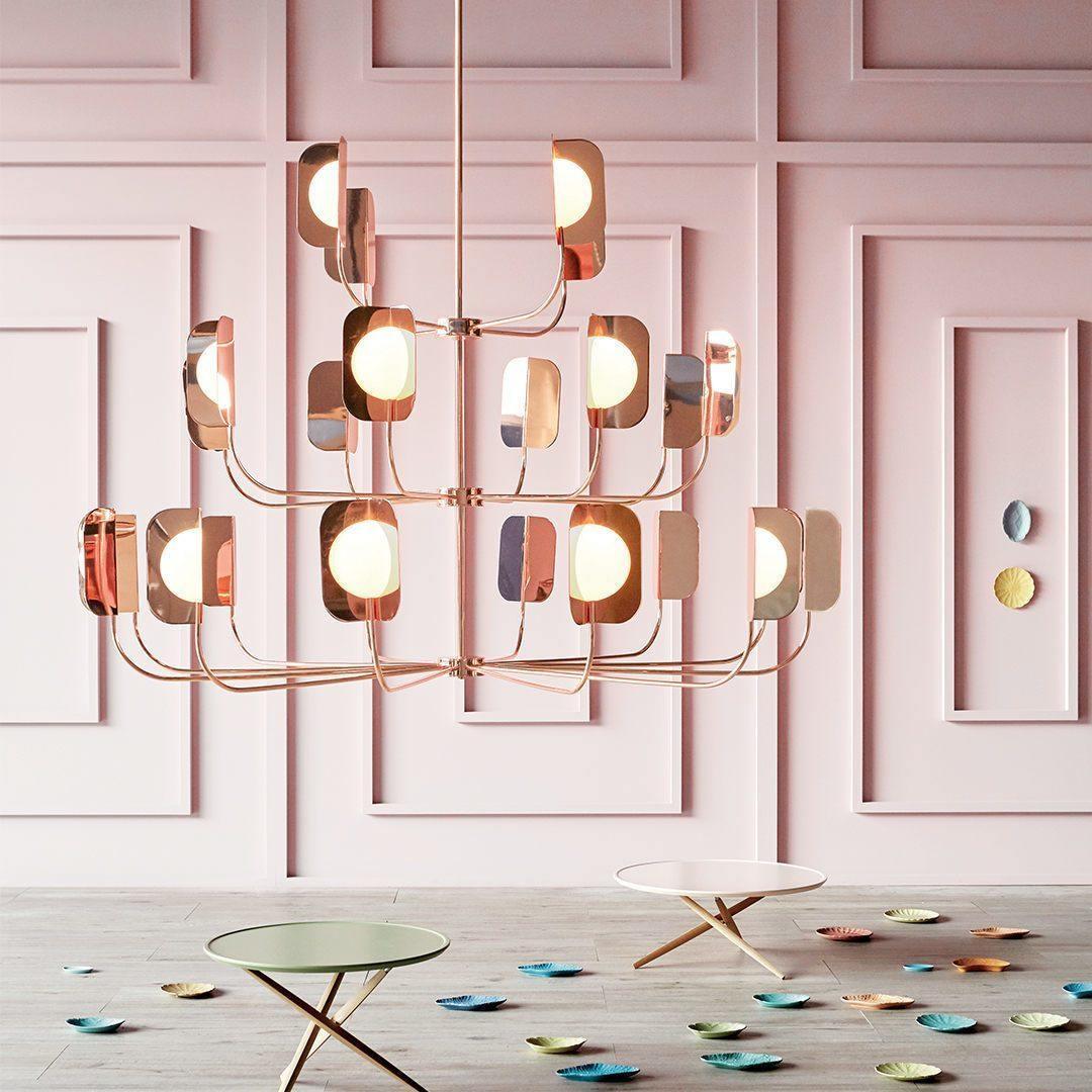 In a pink panelled room, a Clérachic chandelier in a copper finish carries lit globes behind leaf shades above two small side tables.
