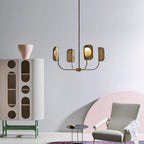 A four-arm Clérachic chandelier in a brass-toned finish hangs beside a tall cabinet with arched cut-outs and a pale grey armchair.