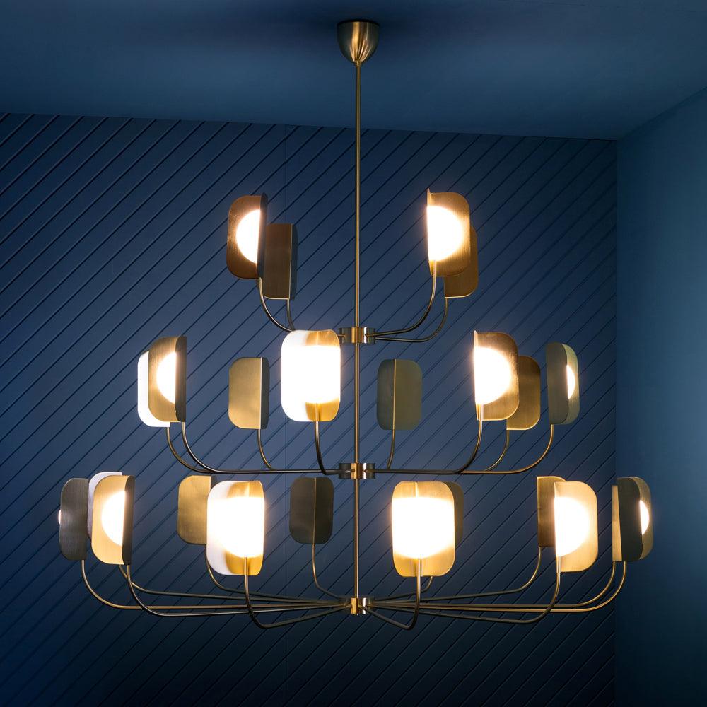 Lit against a deep blue wall, this Clérachic chandelier shows three tiers of brass-toned leaf shades round warm glowing globes.
