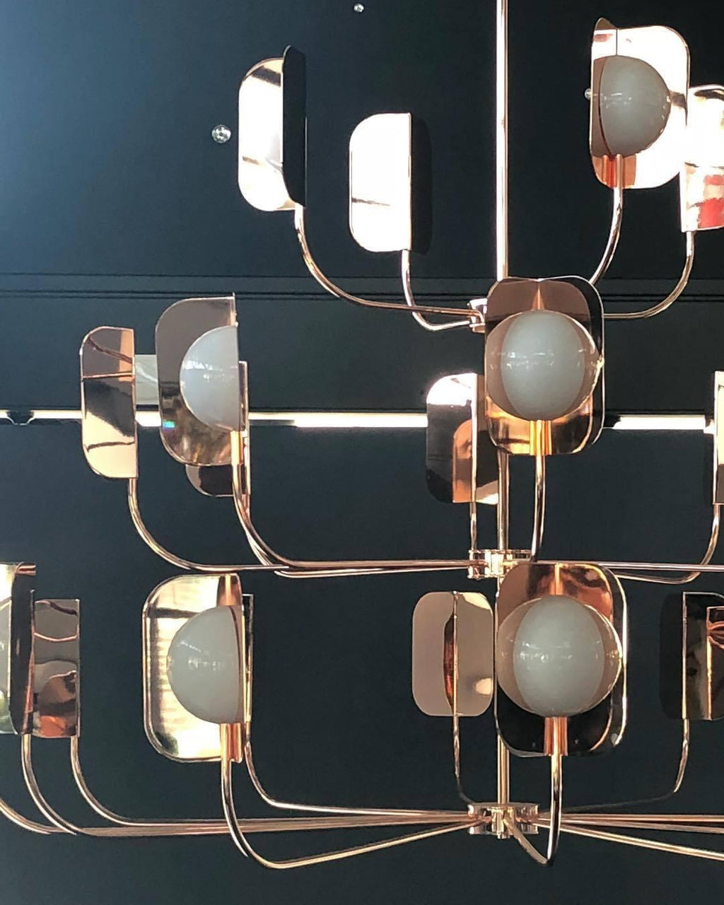 Close view of rose-gold leaf shades, round white globes and slim arms on a Clérachic chandelier, set against a dark teal wall.