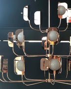 Close view of rose-gold leaf shades, round white globes and slim arms on a Clérachic chandelier, set against a dark teal wall.