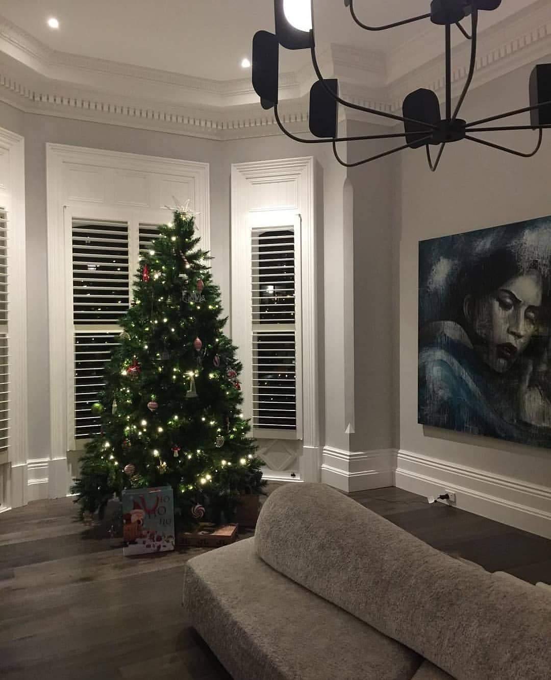 A black Clérachic chandelier hangs in a corner of a grey room with a Christmas tree and a dark painting, seen from below.