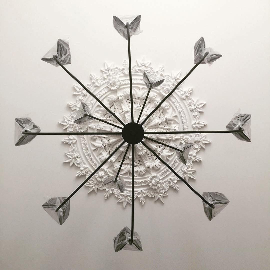 View from below of a black Clérachic chandelier on a ceiling rose, its arms ending in leaf shades wrapped in protective film.
