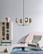 A small brass-toned Clérachic chandelier hangs in front of a tall cabinet with arched cut-outs, a pale armchair and a bright rug below.