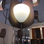 Close view from below of one dark leaf shade round a lit opal globe on a Clérachic chandelier, with other shades blurred beside it.