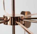 Close view of the copper hub on a Clérachic chandelier, with straight arms radiating from it and one leaf shade blurred behind.