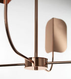 Close view of a copper hub on a Clérachic chandelier, a curved arm leading to a soft-focus leaf shade on a white backdrop.